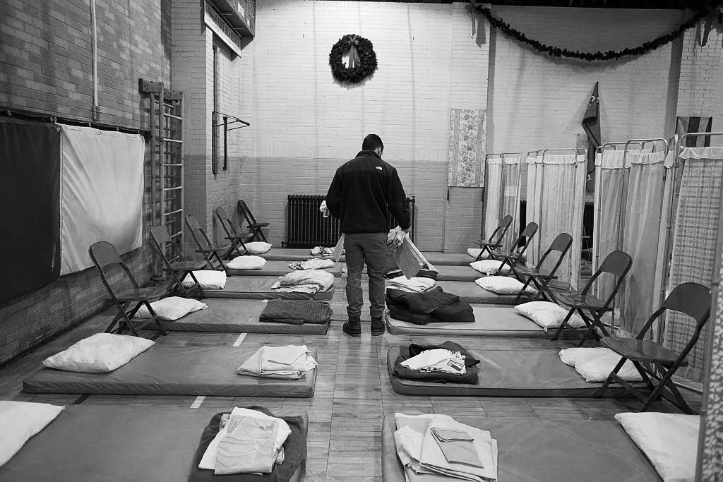 Man putting blankets on a cot in a homeless shelter