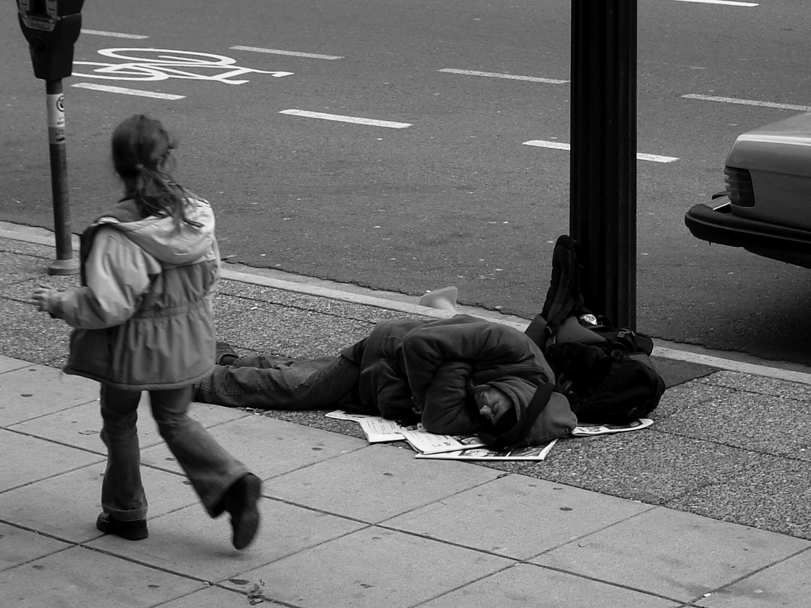 Young girl walking past man sleeping on the sidewalk